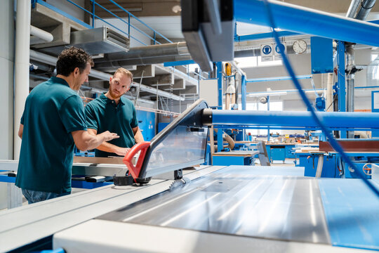Two male carpenters working together next to circular saw in production hall