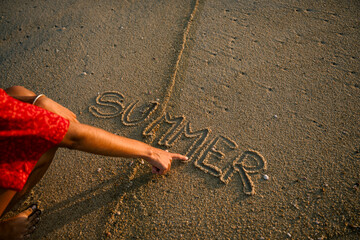 Unrecognizable person writing 'summer' in the sand at the beach