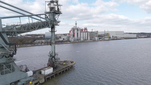 Aerial sweep of riverside industrial zone featuring warehouses, cranes and loading arms projecting over calm water, reflecting large-scale logistics and manufacturing operations