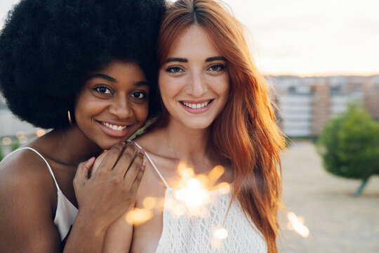 Smiling woman leaning on redhead girlfriend holding sparkler