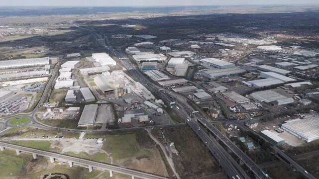 Aerial tracking shot of multilayer A282 interchange with sparse traffic, elevated flyovers and warehouse roofs framing industrial landscape, Thurrock, Essex, UK, March 2025