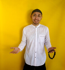 Cheerful Asian Muslim Man Showing Open Hands Gesture Welcoming Guest While Holding Prayer Beads. Studio Shot