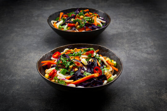 Colorful udon noodle bowls with miso butter vegetables and peanuts on dark background