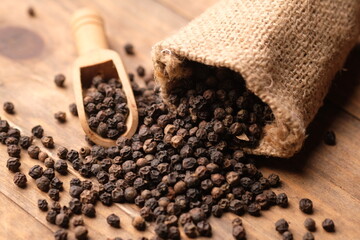 black pepper in a burlap sack on wooden bowl. Pepper, which has the Latin name Piper nigrum, is a...