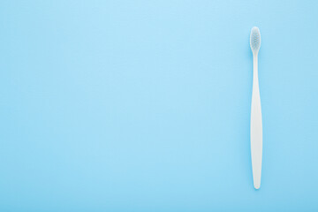 New white toothbrush with soft bristles on light blue table background. Pastel color. Closeup. Empty place for text. Top down view.