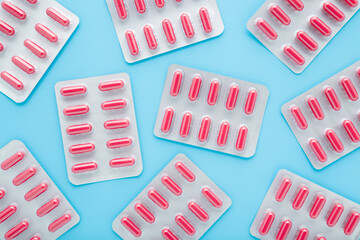 New blister packs of red capsule pills on light blue table background. Pastel color. Closeup. Medicine pattern. Top down view.