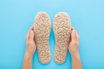 Young adult woman hands holding and showing new light soft natural sheep wool insoles on light blue table background. Pastel color. Closeup. Point of view shot. Top down view.