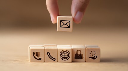 A hand is poised above a natural wood cube, gripping it gently. Symbols of communication adorn nearby cubes, reflecting the essential tools of connectivity in contemporary life