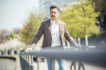 Businessman walking with bicycle by railing on sunny day