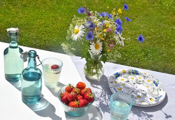 Wildflowers, glasses with a refreshing drink with strawberries on a table in Midsummer in the garden.