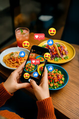Person holding a smartphone photographing a colorful table of pasta, tacos, and salad with floating likes, hearts, and emoji icons for a vibrant social media post.