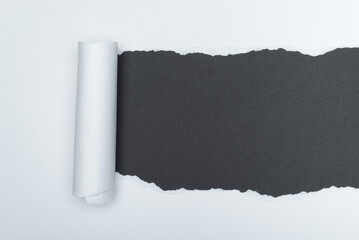 A piece of white paper is torn to reveal a dark gray background