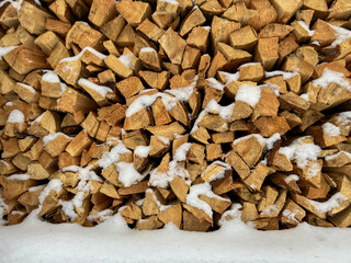 Pine wood cut and split into pieces stored in a pile with a small amount of snow, as winter firewood. Close-up as background