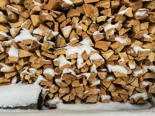 Pine wood cut and split into pieces stored in a pile with a small amount of snow, as winter firewood. Close-up as background
