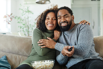Portrait of a happy young couple watching tv together at home. Shot of a couple resting on the couch watching television