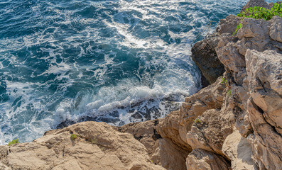 Ocean waves crash energetically against a rocky cliff, creating a powerful and dynamic display of foamy white water and natural force.