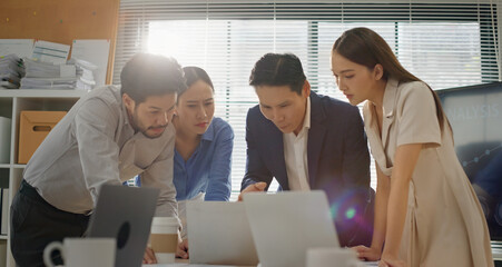 Multicultural business team gathered around laptop in modern office, focused on analyzing data, reviewing project strategy, collaborating on decision making with professional teamwork. Dolly zoom in.