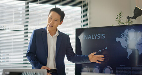 Asian executive presents business data and growth analytics on screen to diverse corporate team during strategy meeting. Multinational group focuses on digital performance, sales, and planning.