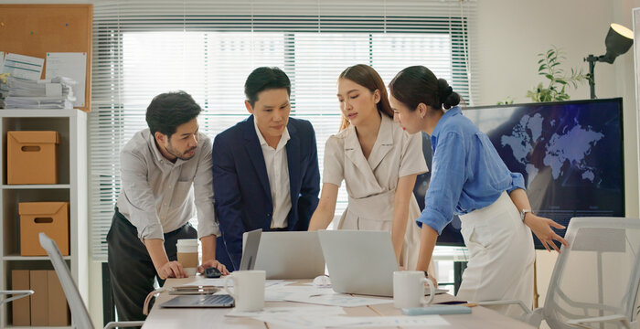 Multicultural business team gathered around laptop in modern office, focused on analyzing data, reviewing project strategy, collaborating on decision making with professional teamwork. Dolly zoom in.