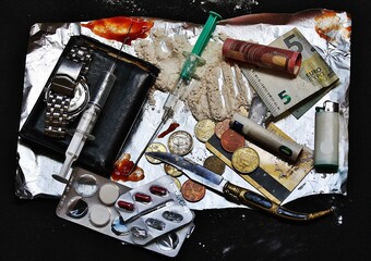 Adicciones de consumo con droga, jeringa, pastillas, dinero, sangre y navaja sobre papel de plata