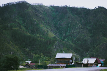 Peaceful summer landscape with green mountains and small village houses near Chemal, Altai Republic, Russia. Concept of rural living, nature retreat, eco lifestyle and countryside relaxation