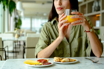 Businesswoman drinking orange juice and eating cheese, cold cuts and small savory pies in a restaurant