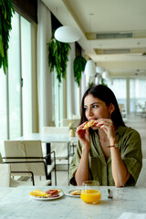 Young woman enjoying a delicious pastry and sipping fresh orange juice while having breakfast in a stylish hotel restaurant