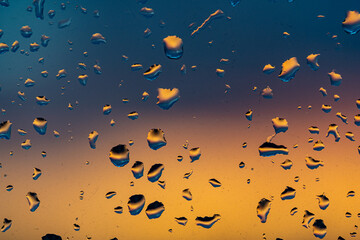 Raindrops on the window against the background of the setting sun. Background with glass and drip...