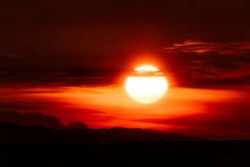 Golden sun dipping below the horizon, painting the sky in fiery orange and red over a dark...