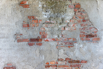 Weathered concrete wall with peeling plaster revealing red brick underneath, featuring cracks,...