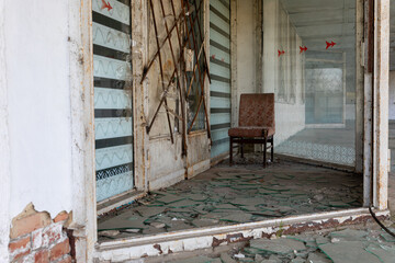Interior of an abandoned storefront featuring broken glass, rusted metal bars, and a worn chair,...