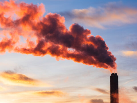 Red smoke emitting from chimney under cloudy sky