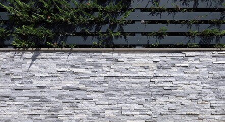 Detail of fence made of white and gray  faux stone paneling wall with black metal slats and hedge...