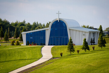 A tall modern chapel with a white cross atop, set on manicured hills in the Ukrainian countryside. Glass facade reflects sky and trees