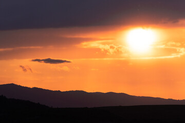 Golden hour sunlight illuminates the silhouette of distant mountains under glowing clouds