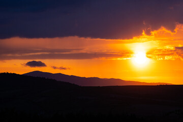 Sunbeam breaks through clouds at twilight above a mountain horizon in vivid tones