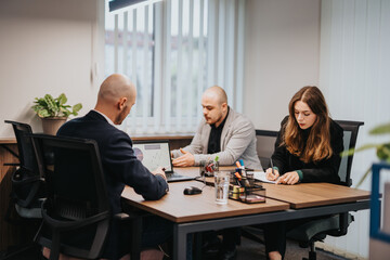 Colleagues working together in a meeting room, analyzing data on a laptop and taking notes....