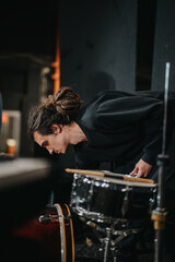 A person adjusts drum equipment on stage, preparing for a musical performance in a live setting.