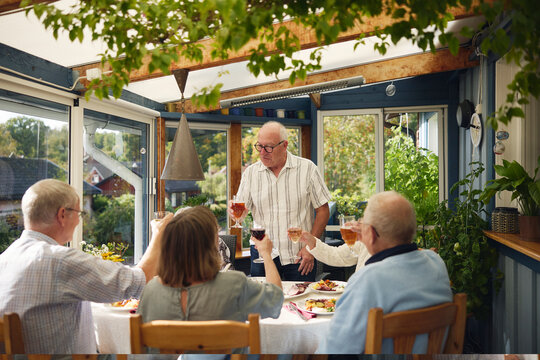 Senior man doing celebratory toast with family friends at patio of house - Powered by Adobe