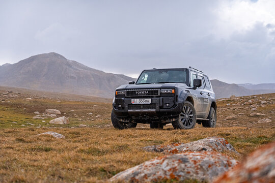 Bishkek, Kyrgyzstan - October 12, 2024: A black Toyota Land Cruiser 250 parked on a brown, grassy field with large mountains in the distance under a cloudy sky