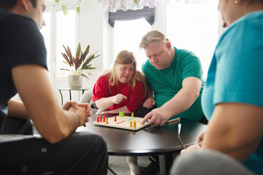 Male and female patients playing ludo game with healthcare workers in nursing home