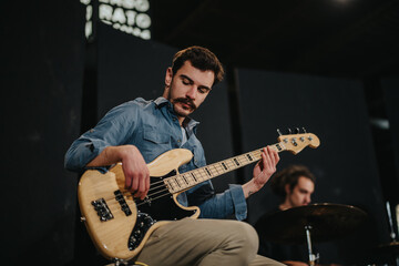 A musician playing an electric bass guitar during a rehearsal in a music studio environment, conveying passion and artistic dedication.