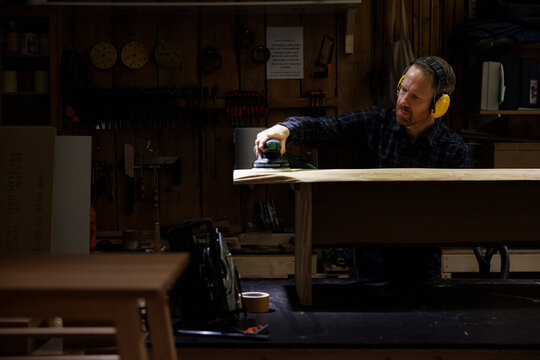 Male carpenter wearing noise cancellation headphones polishing wood in workshop