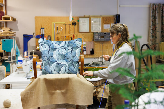 Female upholsterer stitching fabric of arm chair in workshop