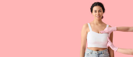 Doctor checking African-American woman's breast on pink background. Cancer awareness concept
