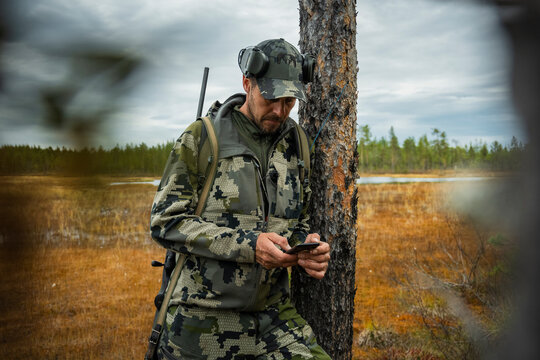 Male army officer wearing military uniform using smart phone while standing near tree