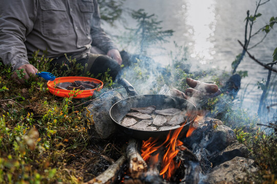 Midsection of man roasting meat in cooking pan on fire