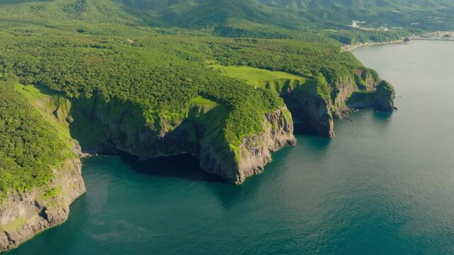 Aerial fly above waters and green rocky coast in Shiretoko Peninsula, Hokkaido, Unesco National Park