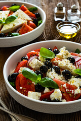 Greek style salad - tomatoes with feta cheese and black olives on wooden table