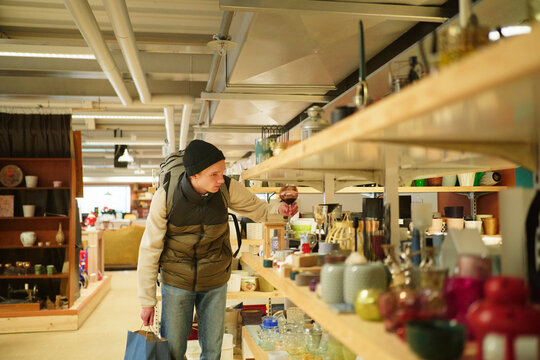 Young man choosing glass from shelf while shopping in store